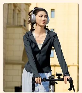 Asiatisches Model in figurbetonter Yoga-Jacke mit Kapuze beim Radfahren mit Kopfhörern.