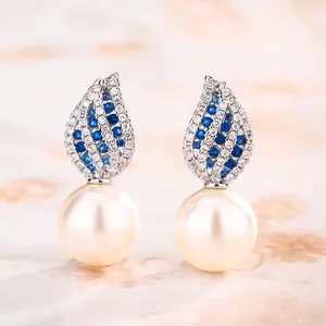 Eleganti orecchini pendenti di perle con pietre blu e bianche su sfondo floreale.