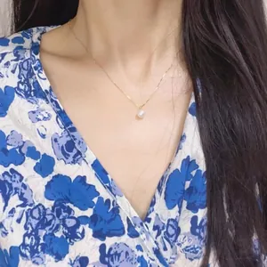 Dettaglio di un elegante collana con perla singola su catena dorata indossata da una modella.