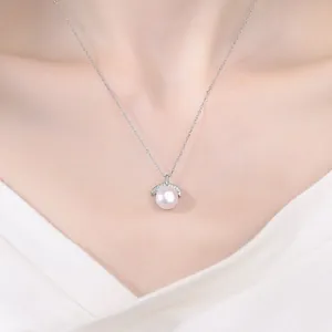 Dettaglio elegante della collana con perla sul collo di una modella in abito bianco.