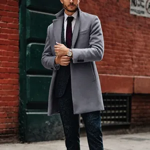Hombre elegante con una gabardina gris de lana de largo medio ante una pared de ladrillo