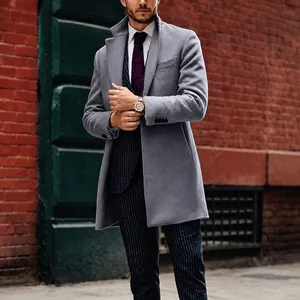 Modern man wearing a grey mid-length wool trench coat against a classic red brick wall