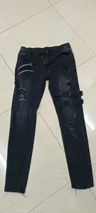 Vista detallada de vaqueros negros rotos para hombre con cremalleras y correas
