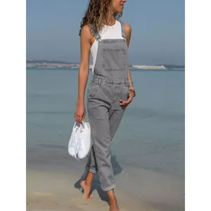 Casual grey denim overalls for women styled with a white top on a sunny beach background