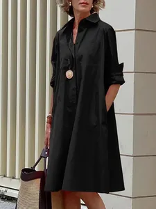 Elegant woman wearing a black cotton linen loose button-down midi shirt dress outside.