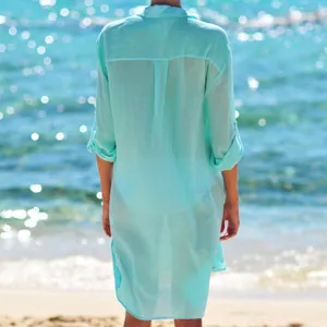 Back view of a turquoise wrinkle fabric beach cover-up shirt on a sunny beach