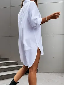 Detail of a white long-sleeved oversized cotton shirt dress featuring high side slits