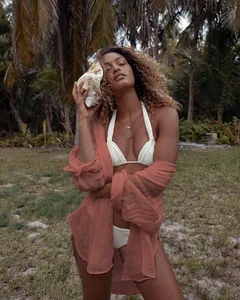 Camisa playera roja óxido en tela arrugada sobre bikini blanco en un entorno tropical