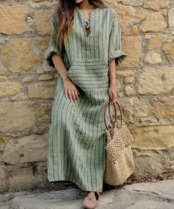 Vue détaillée d'une robe longue bohème rayée en coton et lin contre un mur en pierre.
