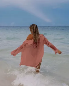 Vista trasera de una camisa de playa rosa palo usada sobre el bañador frente a las olas