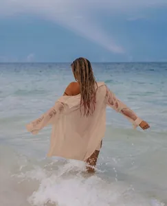 Vista trasera de una mujer caminando hacia el mar con una camisa playera ligera color beige