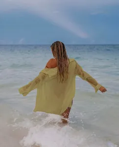 Modelo luce una camisa de playa amarillo claro de tela arrugada en las olas del mar