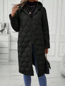 Detail of a woman wearing a black quilted hooded long coat in a minimalist room