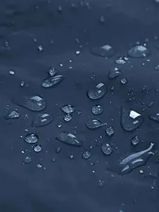 Macro close-up showing water droplets on a dark blue waterproof outdoor jacket fabric surface