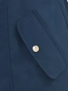Détail du rabat de poche et du bouton métallique sur un trench imperméable bleu marine