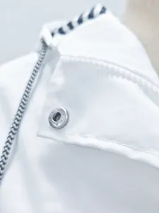 Détail d'un col de veste d'extérieur blanche imperméable avec un bouton-pression métallique.