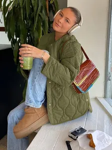 Eine Frau trägt eine gesteppte olivgrüne Jacke, während sie sich in einem Café entspannt.