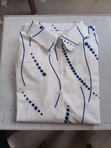 Close-up detail of a folded white women's shirt dress featuring navy blue geometric patterns