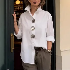Primer plano de camisa blanca con cuello alto y botones metálicos de gran tamaño