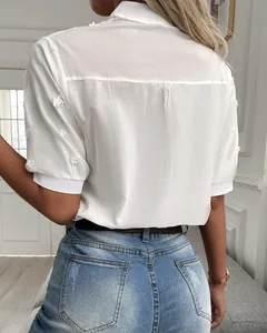 Close-up back view detail of a white short-sleeved embroidered shirt with floral accents.