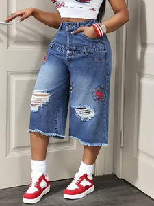 Detailed view of ripped denim capri pants with raw hems and red embroidered S patches