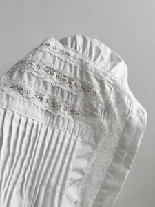Primo piano del pizzo bianco e delle pieghe verticali sulla manica della camicia in cotone