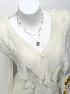 Close-up view of a white ruffled chiffon shirt paired with a heart pearl necklace accessory