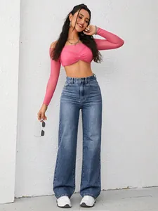 Full body view of a model wearing high-waisted wide-leg blue jeans against a white wall
