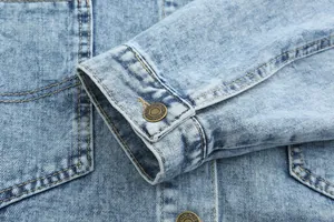 Macro detail of a light blue vintage denim jacket sleeve with embossed metal button