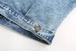 Close-up of a vintage wash blue denim jacket hem featuring an embossed brass metal button
