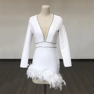 Detail of white bandage dress featuring deep V-neck with rhinestone trim and feather hem