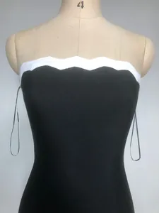 Dettaglio di un abito a fascia bandage nero con bordo smerlato bianco sulla scollatura