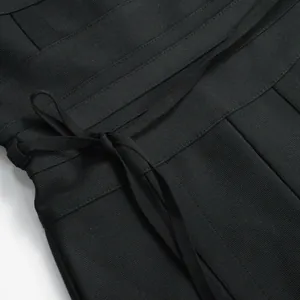 Close-up of the black ribbed bandage fabric and waist tie detail on the jumpsuit