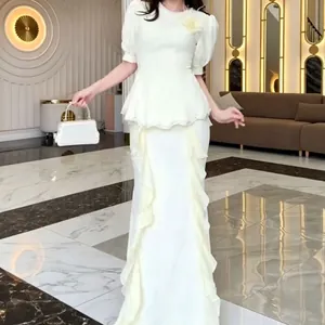 Elegant white peplum fishtail dress with ruffle details in a luxury indoor setting.