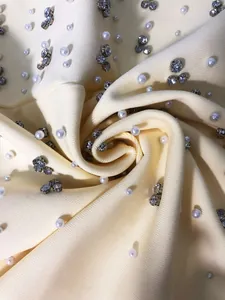 Close-up of high-end cream bandage fabric with pearls and rhinestones for evening dress