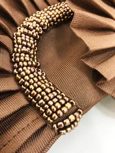 Detailed close-up of handmade metallic beadwork on elegant bronze bandage dress