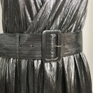 Primer plano de vestido plisado metalizado con cinturón ancho y hebilla a juego
