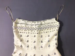 Detailed close-up of heavy rhinestone and pearl embellishments on cream bandage dress