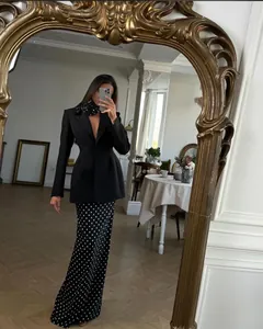 Elegant model wearing black polka dot suit set in front of an ornate gold mirror detail