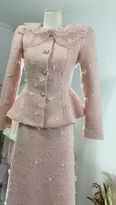 Detailansicht des rosa Tweed-Zweiteilers mit 3D-Blumenapplikationen und Spitzenkragen.