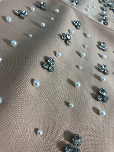 Close-up macro detail of hand-applied pearls and rhinestones on beige bandage dress