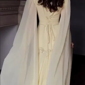 Detail achterkant van een crèmekleurige avondjurk met borduursel en elegante cape mouwen