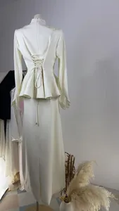 Elegant white peplum suit set with pleated sleeves and lace-up back detail on mannequin.