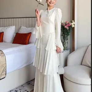 Elegant white tiered long sleeve dress with floral detail shown in a bedroom setting