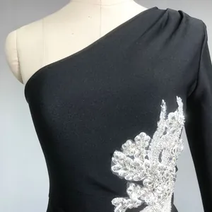 Detail of black one-shoulder bandage dress with sparkling rhinestone flower applique.