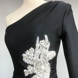 Close-up of intricate rhinestone flower appliqué on black one-shoulder evening dress.