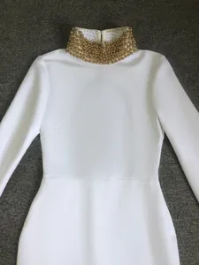 Detailed macro shot of an elegant white bandage dress featuring a gold beaded stand-up collar