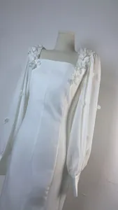 Primo piano di un abito bianco con scollo quadrato e applicazioni floreali 3D sulle spalle