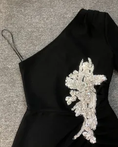 Close-up detail of sparkling rhinestone floral applique on a black one-shoulder bandage dress.
