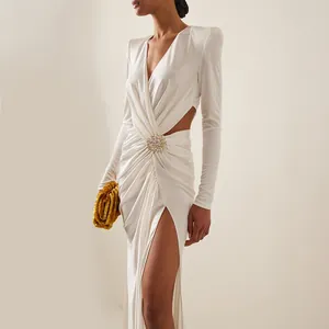 Detail view of an elegant white maxi dress with jeweled brooch and waist cut-out